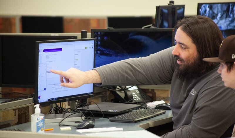 A teacher points at a computer screen while guiding a student, showing how setting clear goals supports learning and progress.