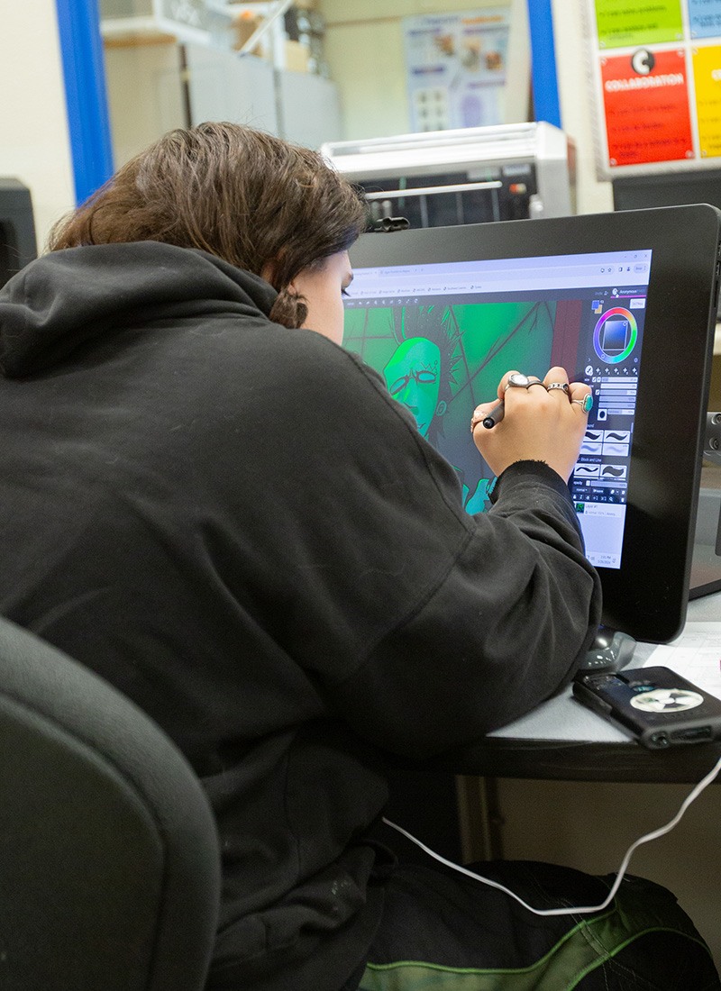 schedule-tour-hero-v1 A student works on digital art using a stylus and drawing tablet, showcasing creativity and focus in a tech-driven classroom