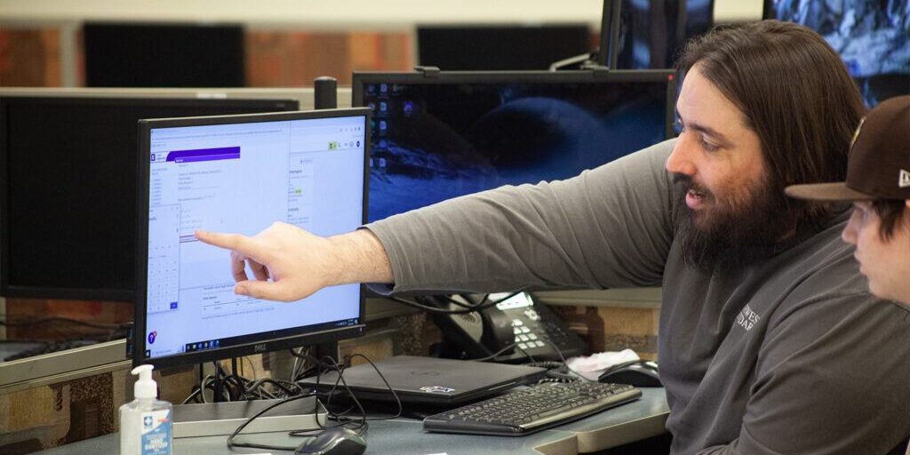 how-to-talk-to-your-teenage-student-about-goal-setting-1500x1000 A teacher points at a computer screen while guiding a student, showing how setting clear goals supports learning and progress.